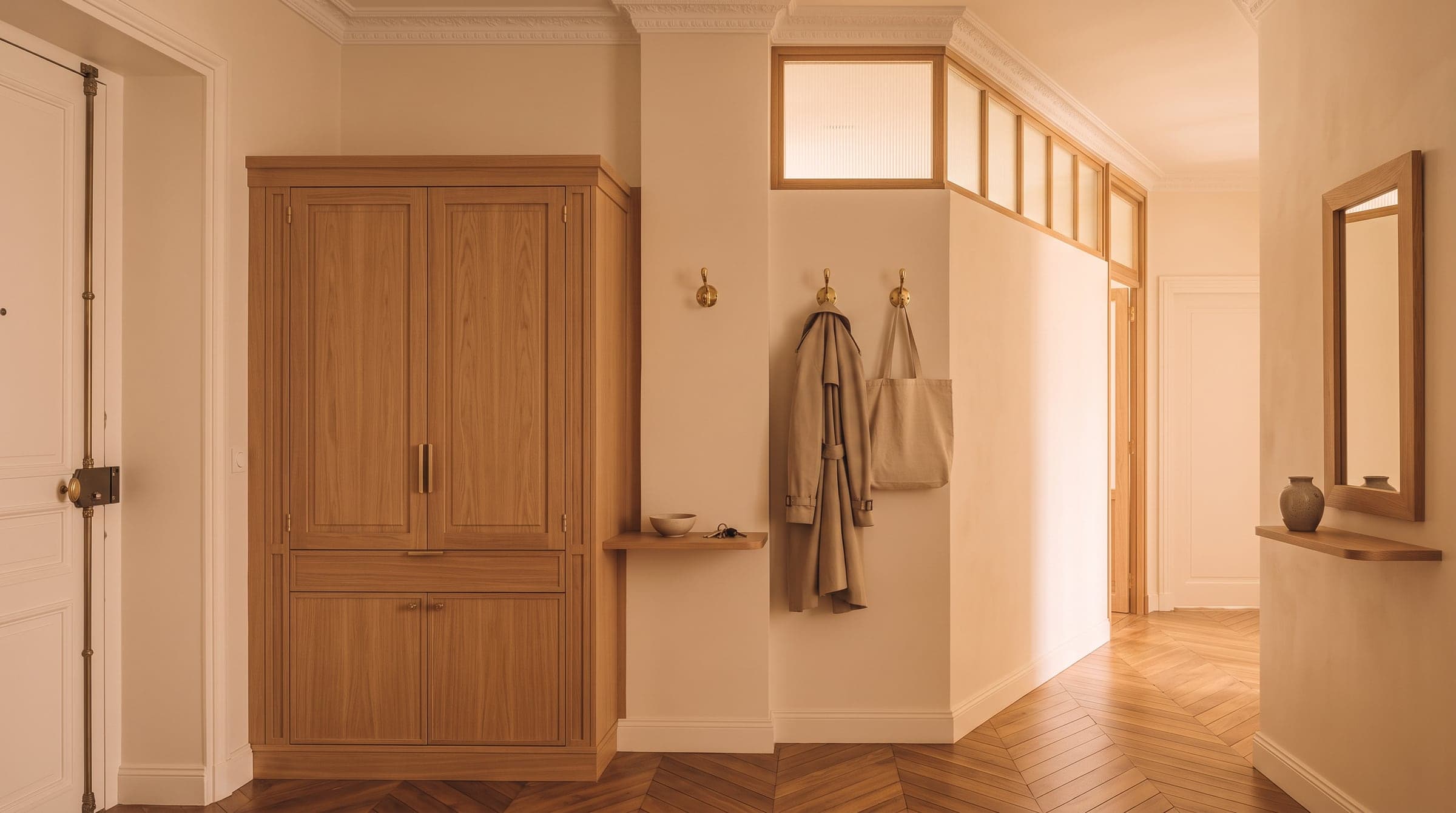 Closed entryway storage with two open hooks beside it holding a coat and a bag near the front door