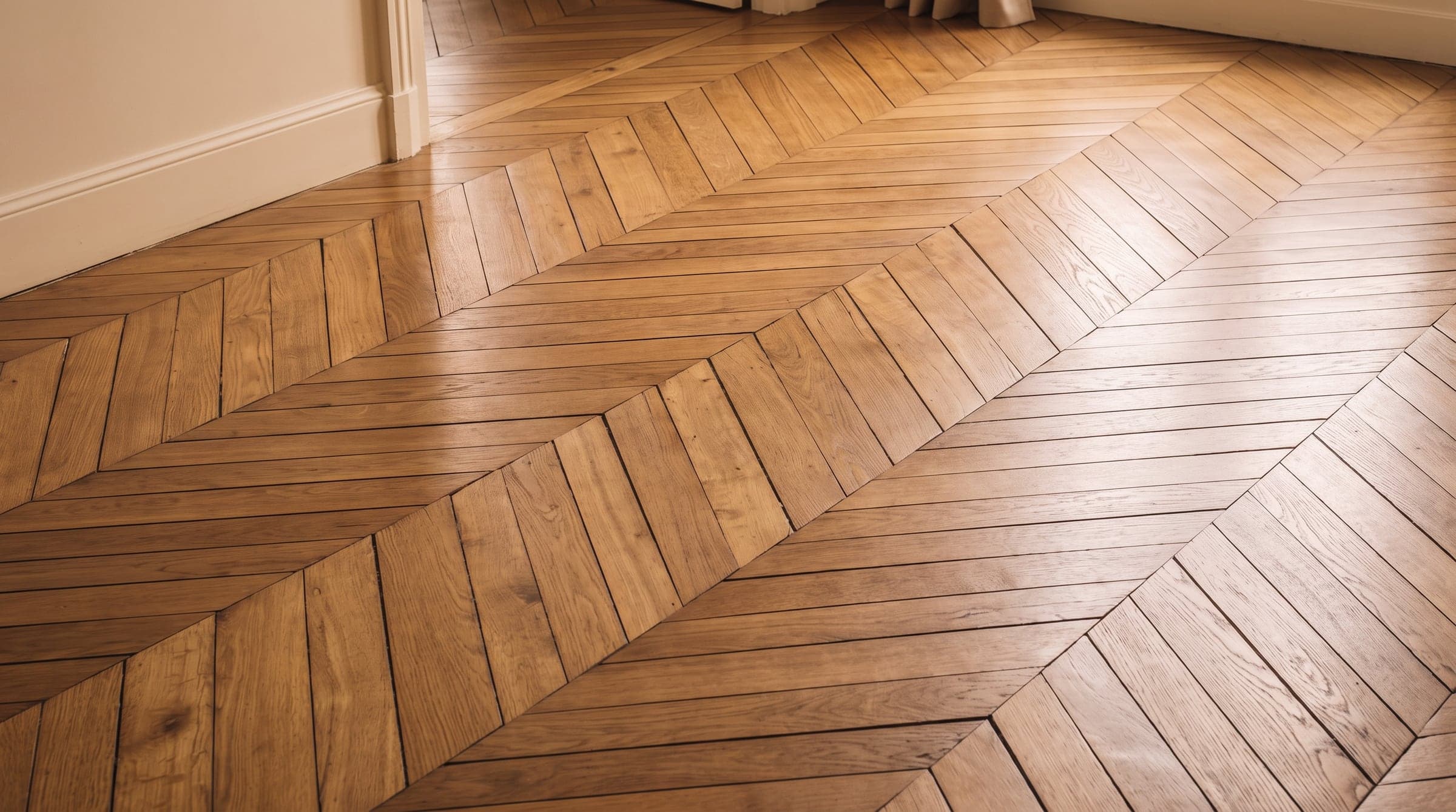 Détail d'un parquet ancien en chêne massif restauré, lames et jours visibles sous une lumière rasante